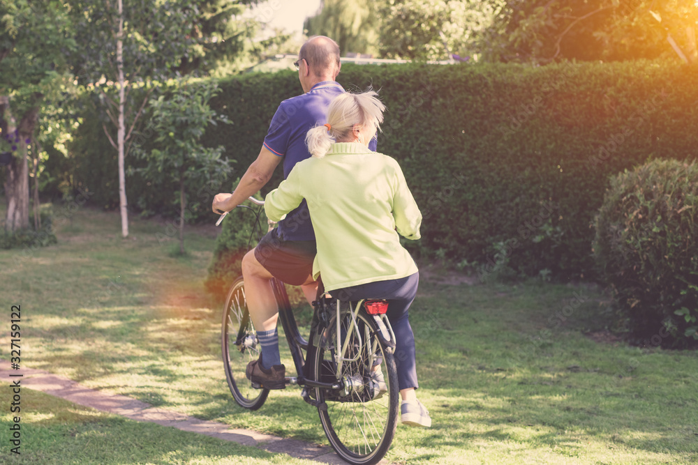 Rear view of senior couple riding a bicycle together - leisure, having fun and ecological transport concept