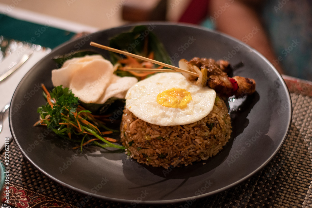 Nasi goreng, a traditional balinese food served during the dinner in a black plate in a restaurant in Bali Nasi goreng, a traditional balinese food served during the dinner in a black plate in a restaurant in Bali