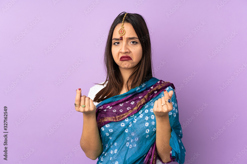 Young Indian woman isolated on purple background making money gesture but is ruined Young Indian woman isolated on purple background making money gesture but is ruined