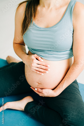 beautiful pregnant girl in sportswear sitting on a yoga Mat and stroking her belly on a studio