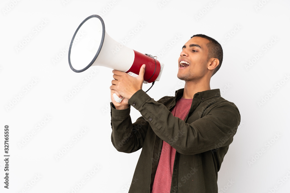 Young African American man over isolated white background shouting through a megaphone Young African American man over isolated white background shouting through a megaphone