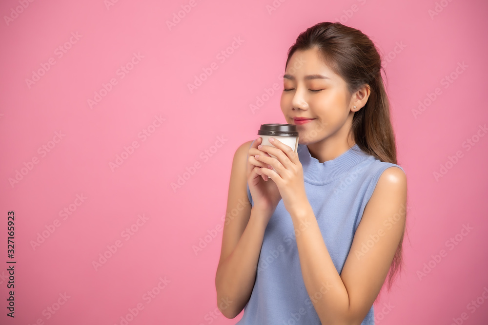 Portrait of a pretty young Asian business woman in sweater using mobile phone while holding takeaway coffee cup isolated over pink background. Portrait of a pretty young Asian business woman in sweater using mobile phone while holding takeaway coffee cup isolated over pink background.