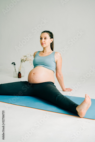 a young beautiful pregnant girl in sports clothes is doing yoga, performing exercises sitting on a rug in the Studio