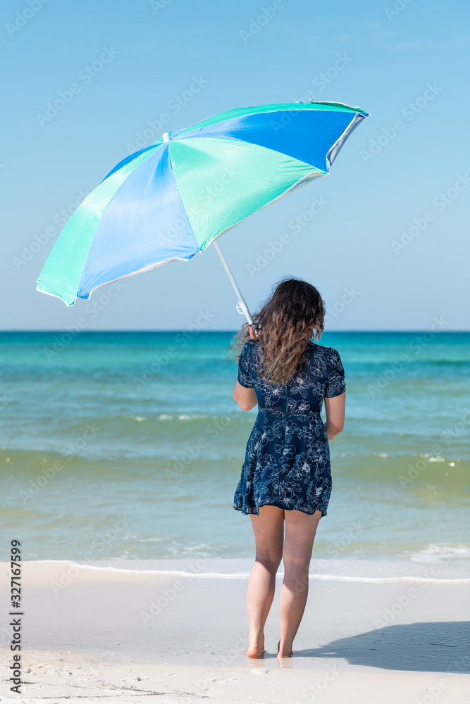 Young girl woman back standing on beach on sunny day with hair in wind in Florida panhandle with ocean on gulf coast