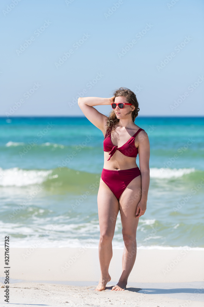 Young girl woman in red bikini bathing suit sunglasses touching hair with ocean sea green water in background in Santa Rosa Beach and horizon Young girl woman in red bikini bathing suit sunglasses touching hair with ocean sea green water in background in Santa Rosa Beach and horizon