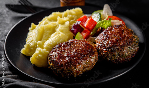 burger with mashed potatoes and vegetables salad on a black plate on Dark grey black slate background photo