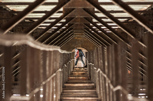 Climber with equipment stands among the converging in perspective lines of rusty  old supports and beams of the bridge.