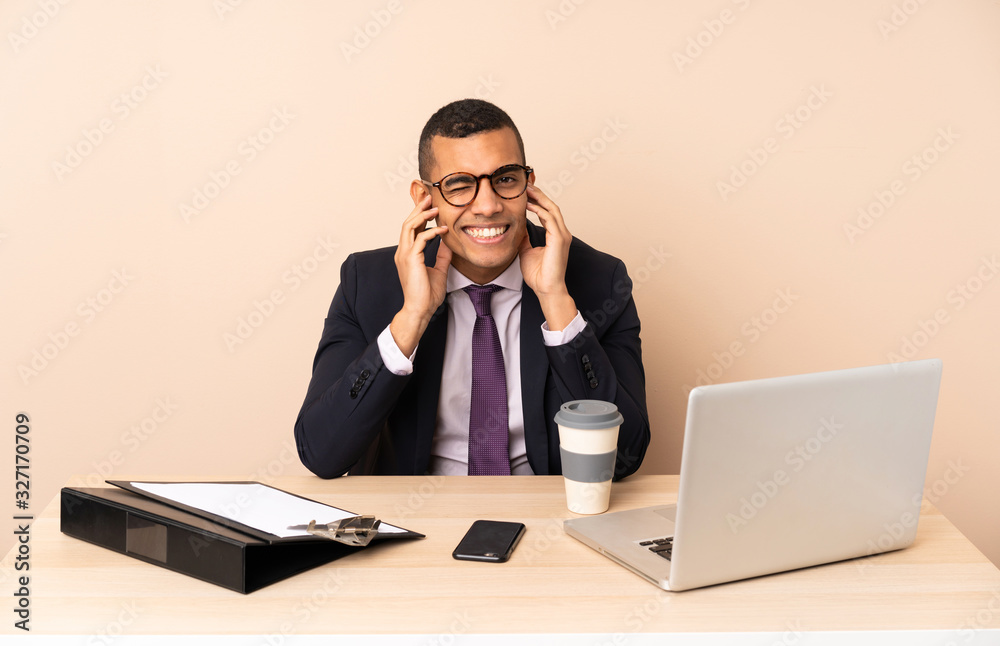 Young business man in his office with a laptop and other documents frustrated and covering ears Young business man in his office with a laptop and other documents frustrated and covering ears