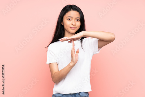 Teenager Chinese woman isolated on pink background making time out gesture © luismolinero
