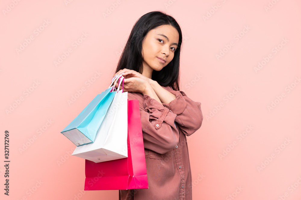 Teenager Chinese girl isolated on pink background holding shopping bags