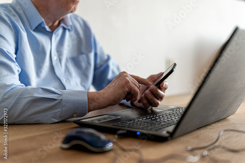 Elderly man who manages his banking affairs online with two-stage verification via laptop and smartphone.