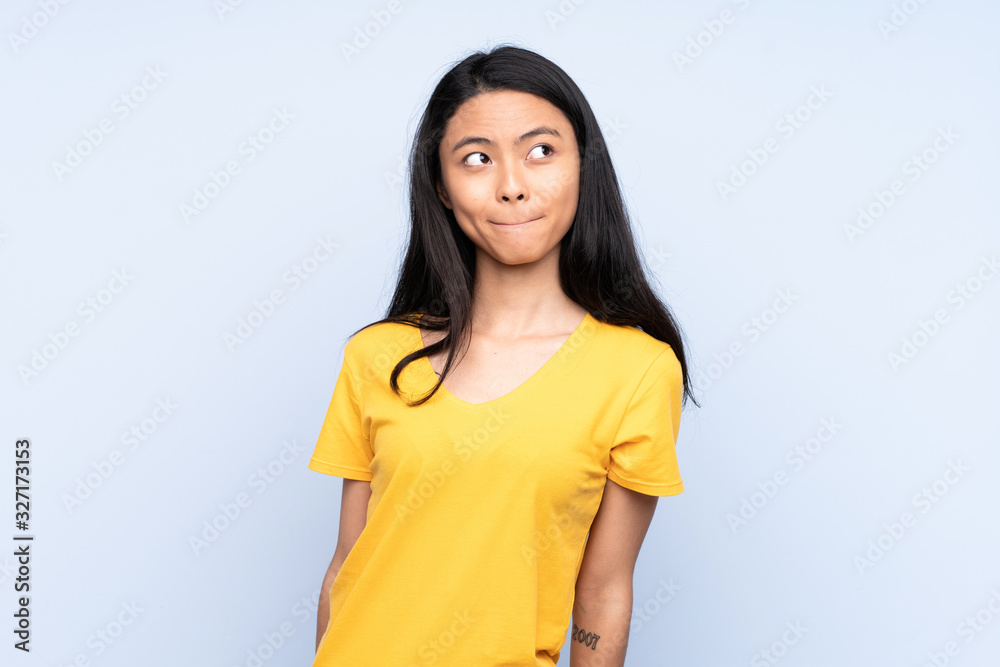 Teenager Chinese woman isolated on blue background having doubts while looking up Teenager Chinese woman isolated on blue background having doubts while looking up
