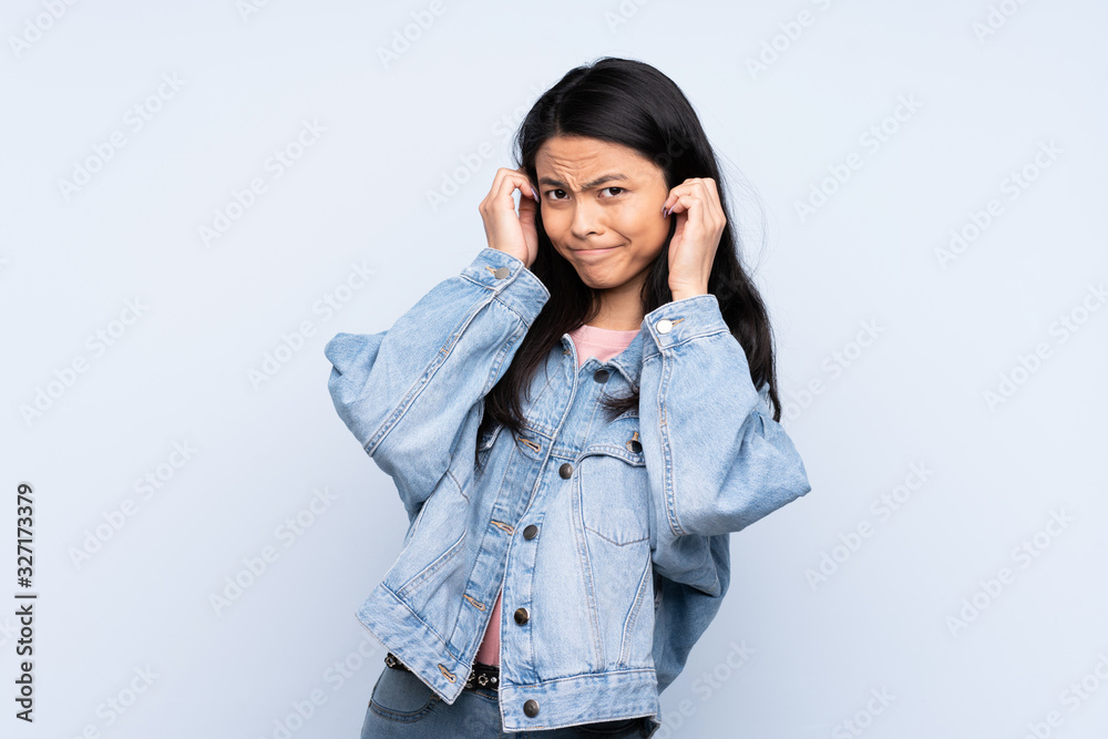 Teenager Chinese woman isolated on blue background frustrated and covering ears Teenager Chinese woman isolated on blue background frustrated and covering ears