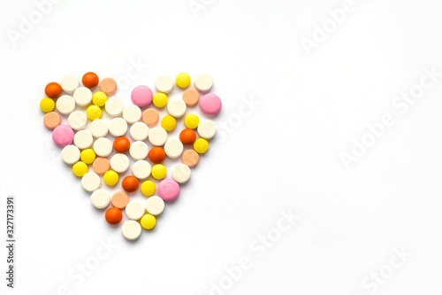 The concept of pills for treatment. Multi-colored white, orange, yellow, pink pills in the shape of a heart on a white isolate background. Copy space