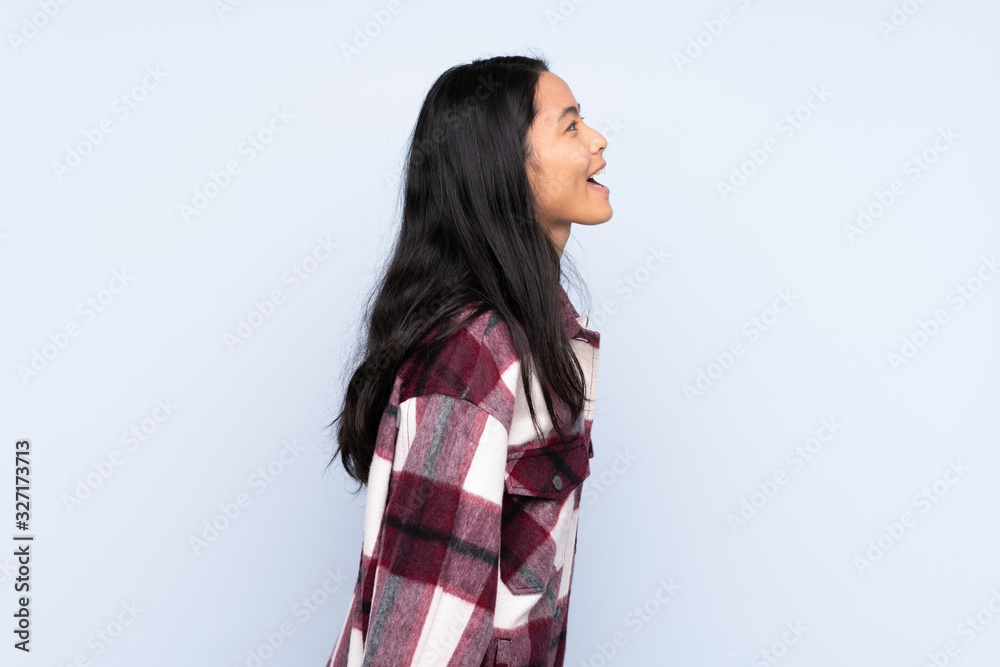 Teenager Chinese woman isolated on blue background laughing in lateral position Teenager Chinese woman isolated on blue background laughing in lateral position