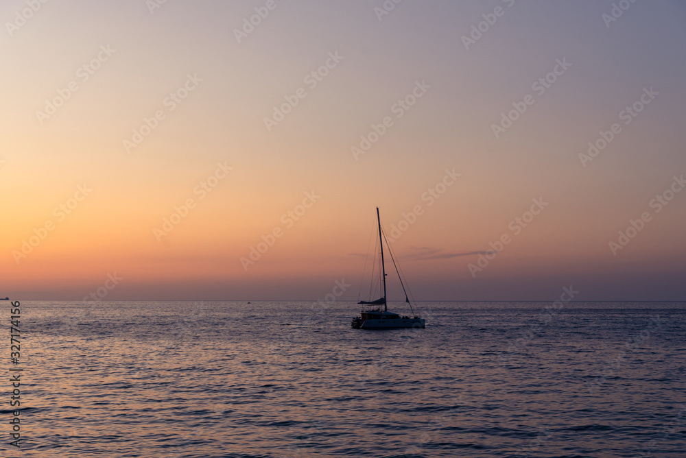 Sunset at sea on a beautiful summer day, with a silhouette of a sailboat
