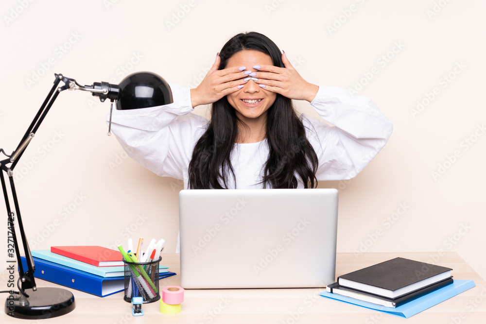 Student asian girl in a workplace with a laptop isolated on beige background covering eyes by hands Student asian girl in a workplace with a laptop isolated on beige background covering eyes by hands
