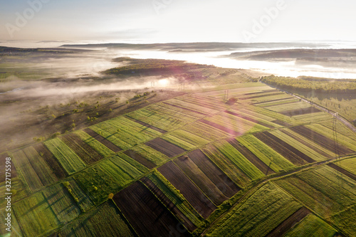 Agricultural landscape from air on sunny spring dawn. Green and brown fields, morning fog.
