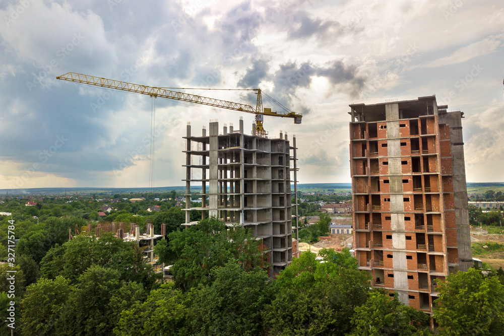 Aerial view of tower lifting crane and concrete frame of tall apartment residential buildings under construction in a city. Urban development and real estate growth concept. Aerial view of tower lifting crane and concrete frame of tall apartment residential buildings under construction in a city. Urban development and real estate growth concept.