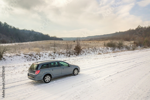 Family car driving on a dirt road in snow covered winter field.