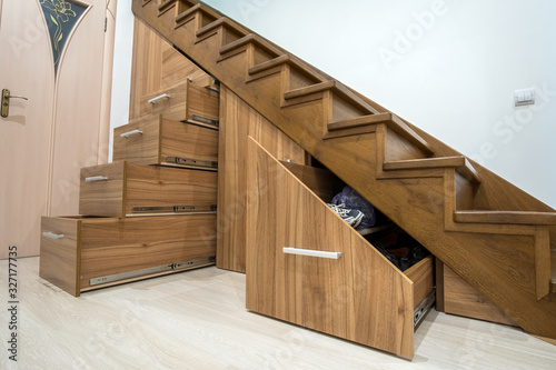Modern architecture interior with luxury hallway with glossy wooden stairs in multi-storey house. Custom built pullout cabinets on glides in slots under stairs. Use of space for storage.