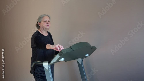 Senior Woman Exercising On Treadmill At Home Wearing Wireless Earphones