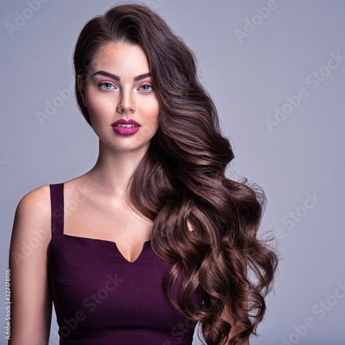 Face of a beautiful woman with long brown curly hair. Fashion model with wavy hairstyle. Attractive young  girl with curly hair posing at studio. Female face with purple makeup. Violet make-up.