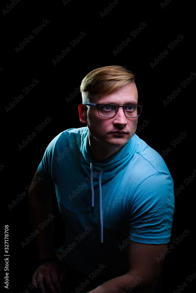 A young man in glasses and a blue T-shirt looks thoughtfully into the distance. A young man in glasses and a blue T-shirt looks thoughtfully into the distance.
