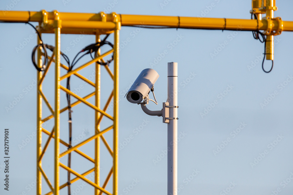 Surveillance camera outdoors in the airport area. Yellow landing light pole in the background. Surveillance camera outdoors in the airport area. Yellow landing light pole in the background.