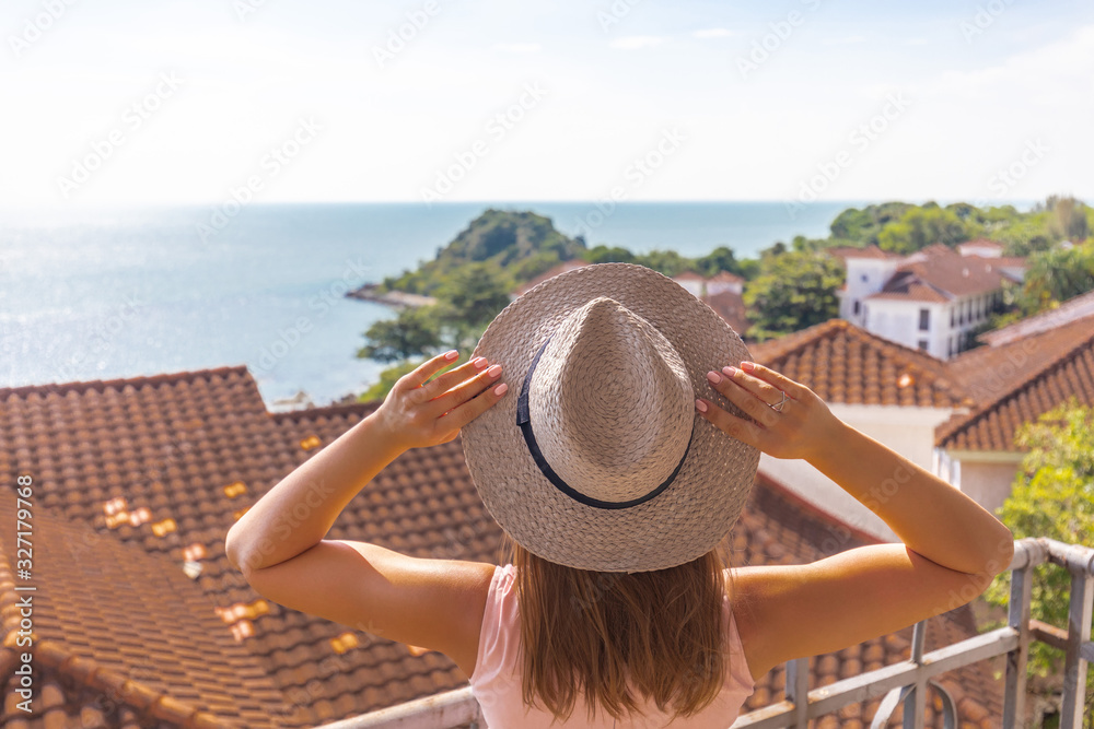 Fototapeta premium girl with a pink dress and hat on the balcony against the sea and tiled roof