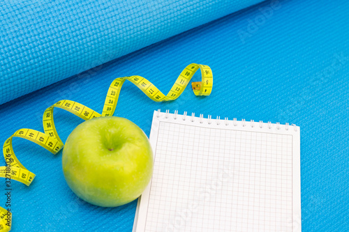 green apple, measuring tape, notebook on a sports mat of blue color. preparation for the summer season and the beach, weight loss and sports concept