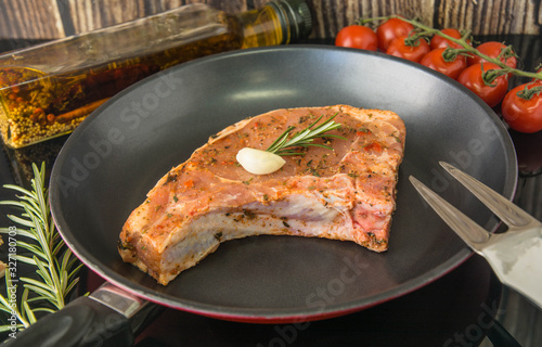 Raw steak with bone in a pan. Induction cooker, tomatoes, rosemary, garlic, meat fork, olive oil.
