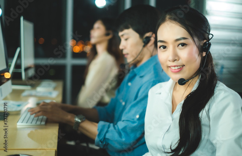 Asian confidence operator woman agent with headsets working in a call center at night Environment with her colleague team as customer service.Successful business people in headsets are using gadgets .