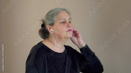 Senior woman exercising on treadmill in the home. Gray hair female use wireless headphones to listen favorite podcast.