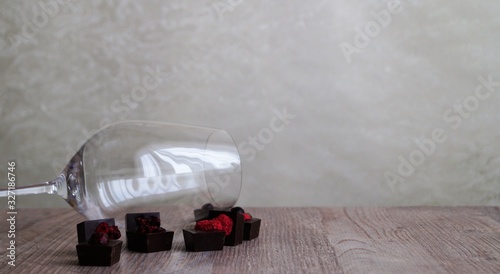 empty wine glass and dark chocolate candies decorated with dried berries on a wooden table on a light background