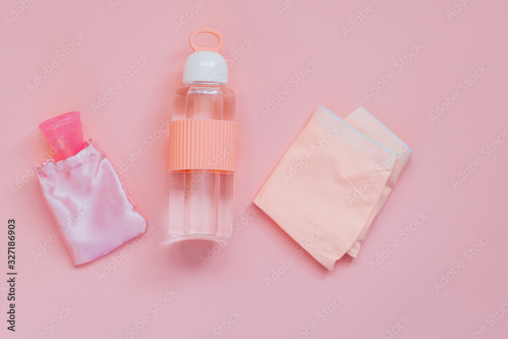 Pink women's panties with menstrual cup notebook with bottle with water. on pink background. Minimalism. Pink women's panties with menstrual cup notebook with bottle with water. on pink background. Minimalism.