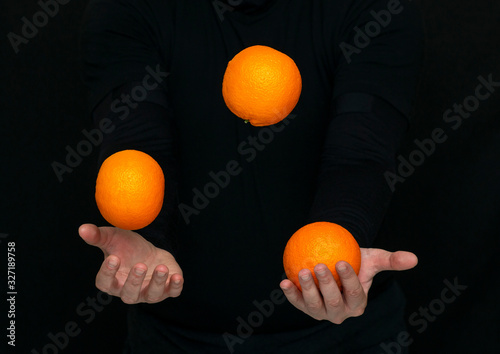 male hands juggle with fresh oranges on a dark background