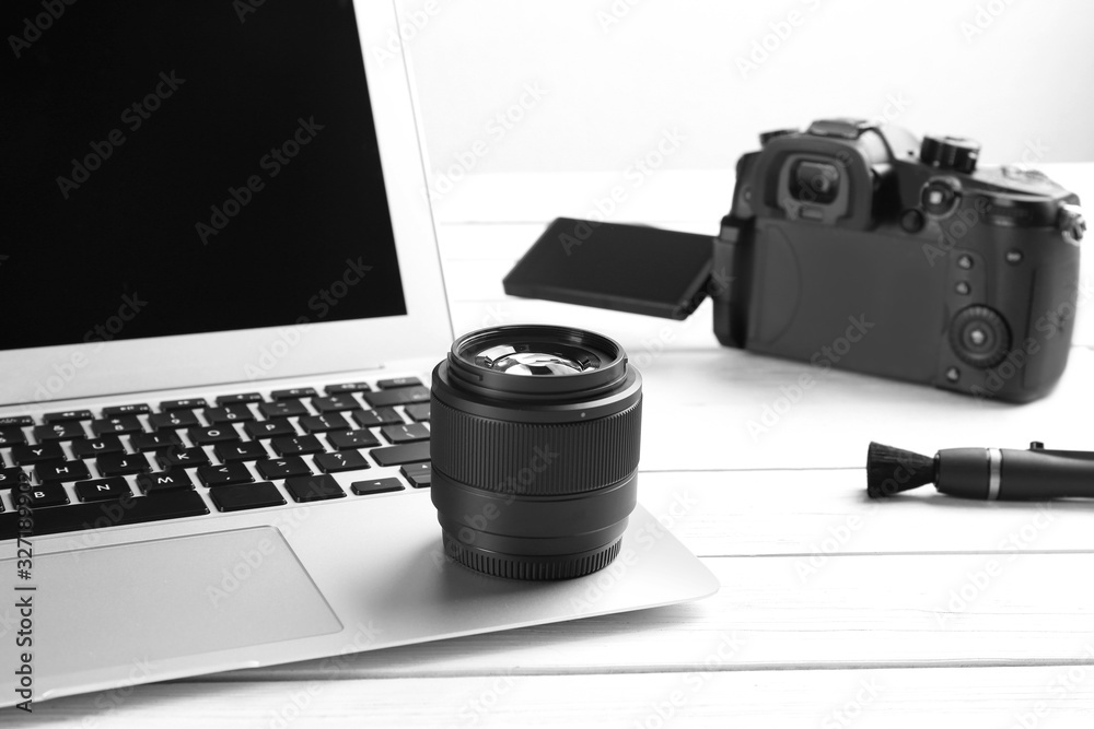 Modern laptop and camera lens on white wooden table, closeup. Video production industry