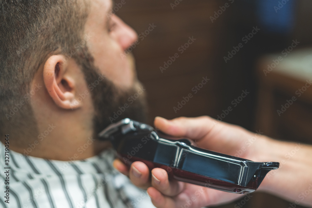 Beauty shop for men. Shaving a beard in a barbershop. Barber cuts his beard with a razor and clipper. close up Brutal haircuts. Hairdresser equipment. Selective focus. Beauty shop for men. Shaving a beard in a barbershop. Barber cuts his beard with a razor and clipper. close up Brutal haircuts. Hairdresser equipment. Selective focus.
