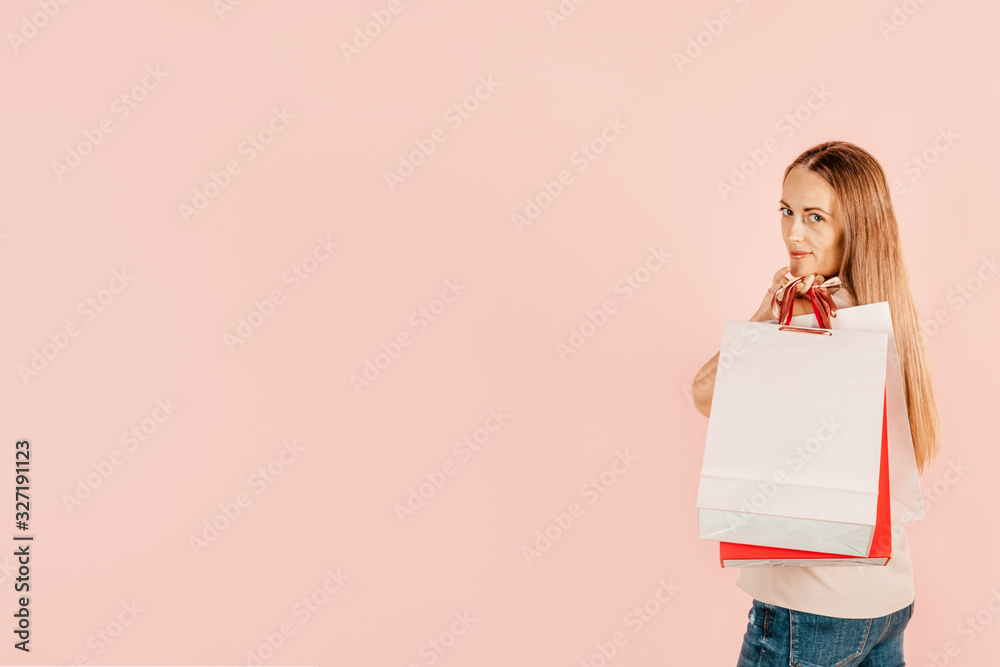 Shopping and consumption. Young and beautiful girl with paper bags for shopping. Pink background. The choice of gifts for the holidays. Shopping for yourself. Mock up Shopping and consumption. Young and beautiful girl with paper bags for shopping. Pink background. The choice of gifts for the holidays. Shopping for yourself. Mock up