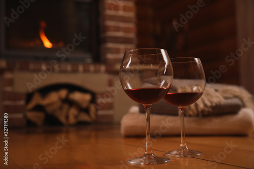 Glasses of red wine on wooden floor near fireplace. Space for text