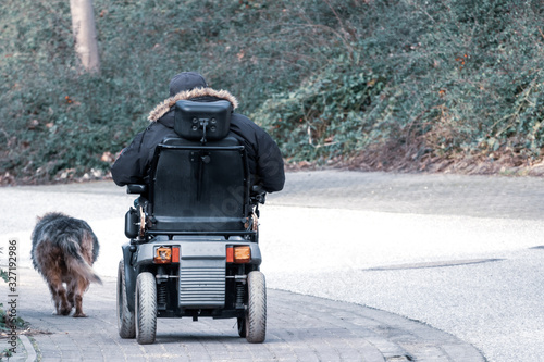 old man drives an electric wheelchair and is accompanied by his faithful dog