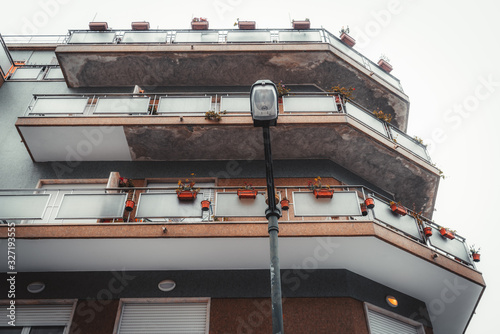 A bottom view of a typical residential building facade with three long balconies with plenty of flower pots on them, tiled walls, overcast sky, street lantern in the foreground, Lisbon, Portugal photo