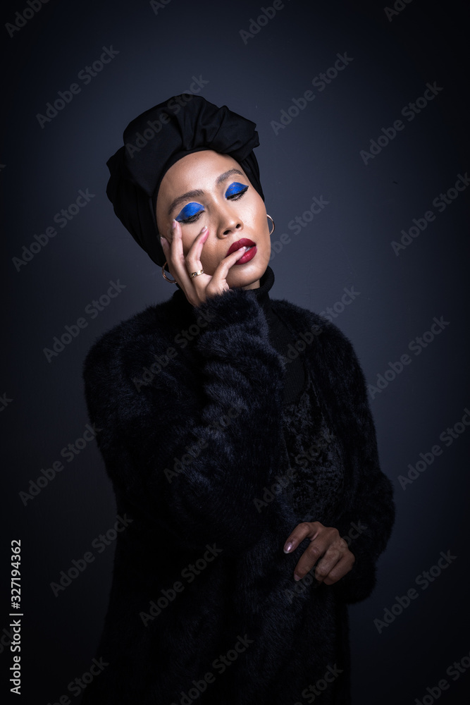 High fashion portrait of an Asian woman in a black top and pants with a turban on grey background. Fashion editorial concept for hijab fashion. Half length