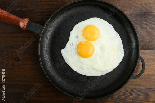 two fried eggs is on the pan on dark wooden background