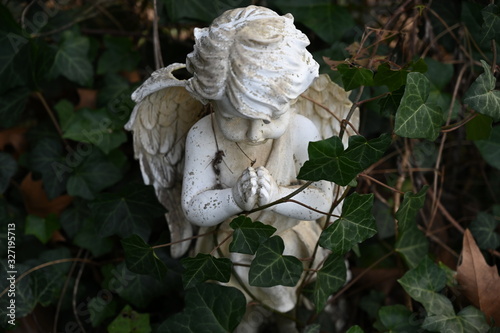 A white statue of a praying angel surrounded by ivy on a tomb of a cemetery in Berlin-Germany.