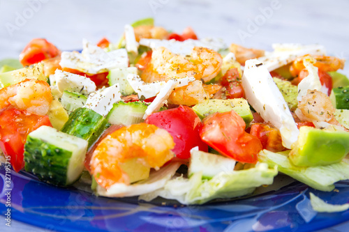 Large glass plate with Greek salad. Tomatoes, cucumbers, avocado, feta cheese, shrimp, salad and spices doused with olive oil