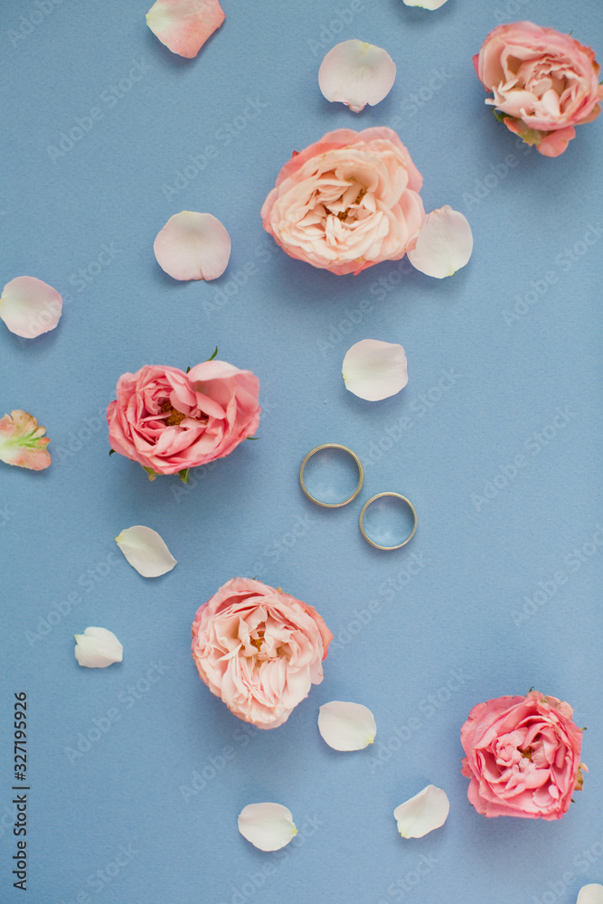 Fototapeta premium Wedding rings near roses and petals on a blue background.