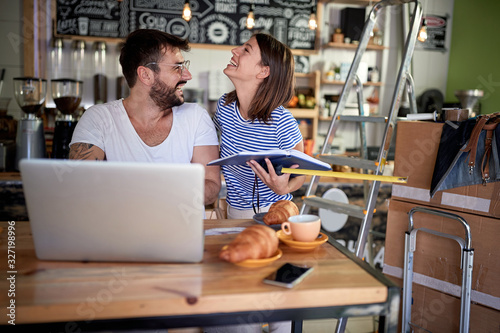 Smiling man working on laptop with his happy girl in their cafe.