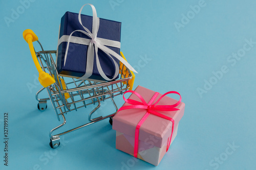 A gift with a white bow in a yellow shopping basket, another gift in a pink box next to it. Selective focus.